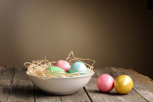Colored easter eggs in nest on wooden table