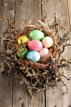 Colored easter eggs in nest on wooden table