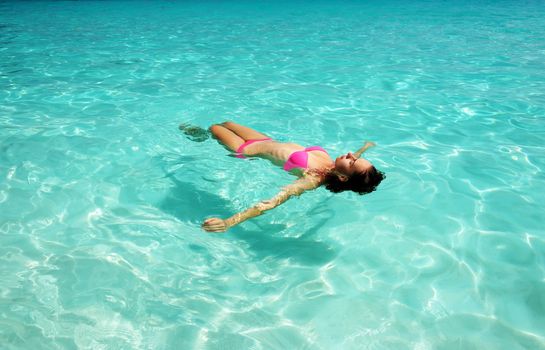 Woman in bikini lying on water at tropical beach