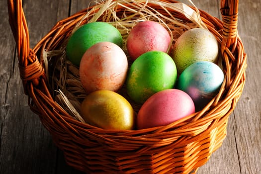 Colored easter eggs in basket on wooden table