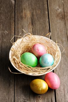 Colored easter eggs in nest on wooden table