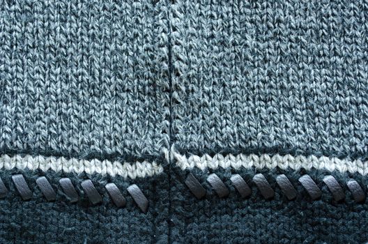 wool knit sweater texture decorated with leather stitch. white grey and black colors backdrop closeup