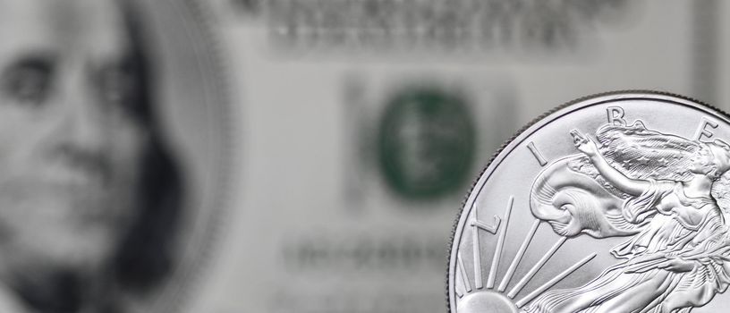 Silver shiny dollar coin on a background of blurry one hundred dollar bill