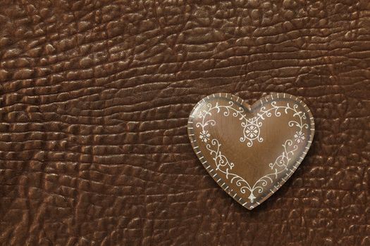 Photo of a metal heart on a dark brown leather background.