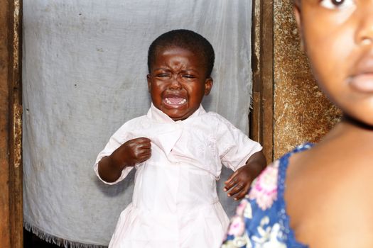 Caught on the fly: little black African baby girl, crying loudly, with bigger sister in the foreground; focus on crying toddler; candid, natural and unstaged portraits.