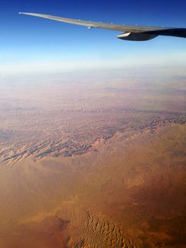 Flying above Africa and its famous Sahara desert, plane wing visible in the sky, earth horizon and beautiful sand dunes and ridges.