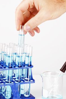 Chemist or other scientist and researcher picking up a test tube filled with blue chemical or liquid, great science background.