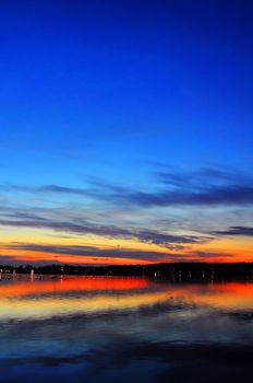 Magnificent sunset over a lake with waterfowl and city lights in a distance, dramatic HDR rendering.