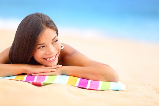 Relaxing beach woman smiling happy looking to the side. Beautiful girl sunbathing under summer sun lying in sand on beach with blue water. Mixed race Asian Chinese / Caucasian female model.
