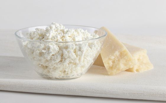 Cottage cheese in the glass bowl with hard cheese on the napkin