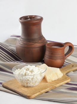 Jug, mug with milk, curds and hard cheese on the tablecloth