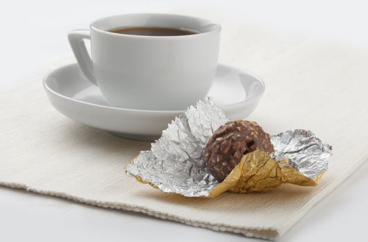 Chocolate candy on the gold foil and cup of coffee on the napkin