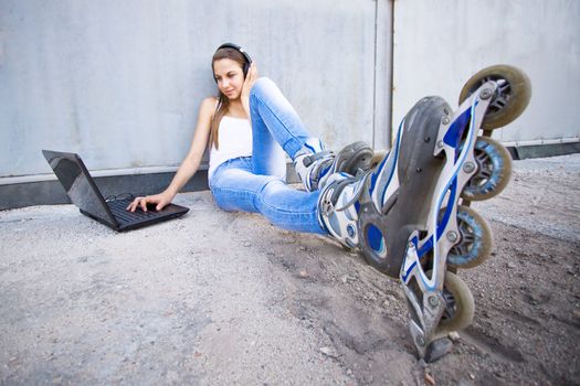 Young girl with laptop, headphones and roller shoes listening to the music