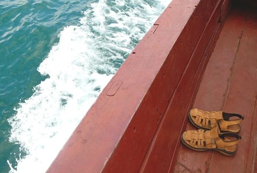 Sandals on boats deck, waves of blue sea