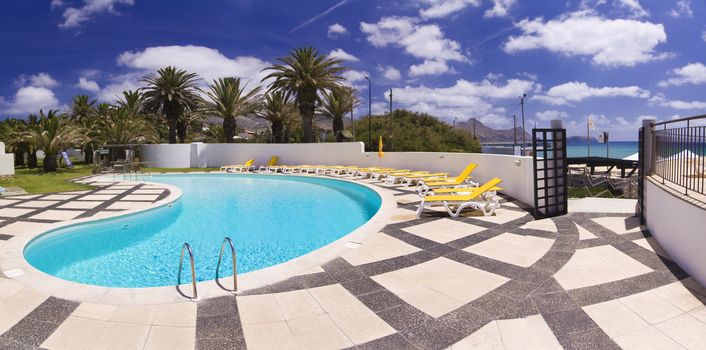 Hotel swimming pool surrounded by deck chairs on the island of Porto Santo, Portugal, panorama