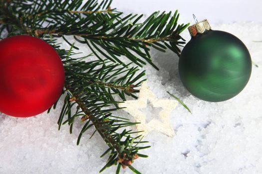 Pine needles and red and green Christmas baubles on snow