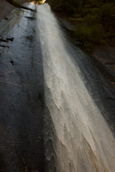 Clean water flowing on a solid gray rock in the shadows