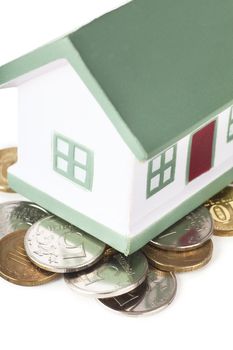 Little house toy on a heap of coins over white background