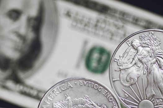 Silver shiny dollar coin on a background of blurry one hundred dollar bill