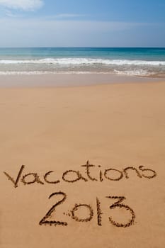 Words "Vacations 2013" written in sand on tropical beach