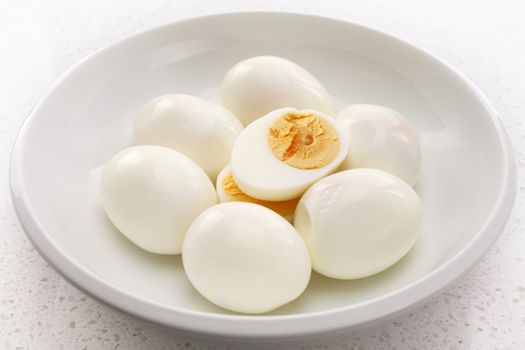 Seven hard boiled eggs in a white bowl, one cut into halves.