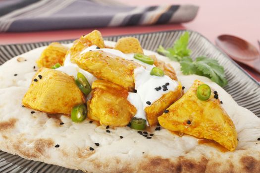 Chicken Madras curry on Indian naan bread, topped with yoghurt, chilli and kalonji seeds.
