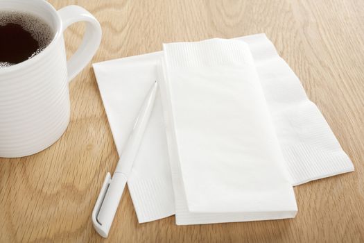 White paper napkin on wooden table with pen for making notes, and mug of coffee, ideal for noting down phone numbers, and that great idea you had at the coffee shop.