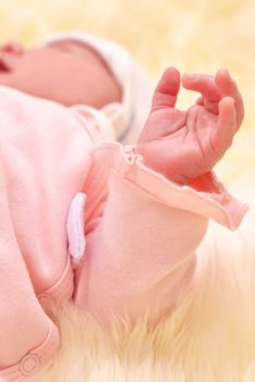 Sleeping baby arm in a pink dress with a blurred background.