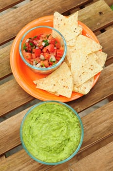Guacamole dip made from fresh avocados, chips and salsa on wood background