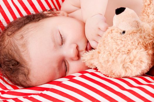 sleeping cute little baby on red and white stripes pillow with teddy bear