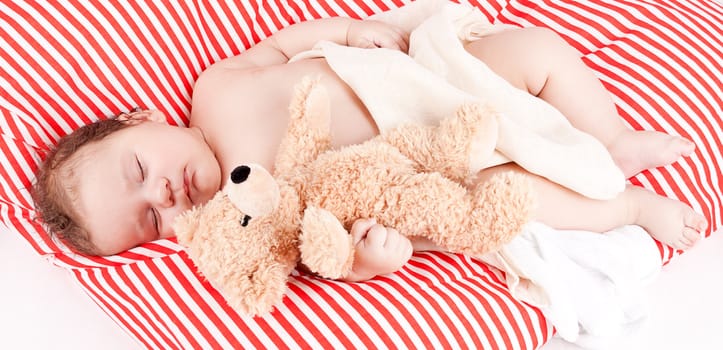 sleeping cute little baby on red and white stripes pillow with teddy bear