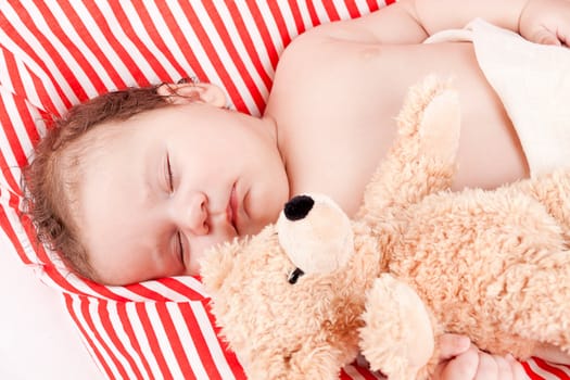 sleeping cute little baby on red and white stripes pillow with teddy bear