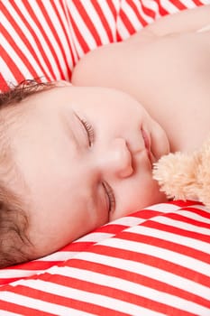 sleeping cute little baby on red and white stripes pillow with teddy bear