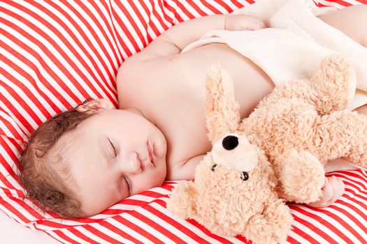 sleeping cute little baby on red and white stripes pillow with teddy bear