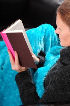 A woman with red hair cuddling up with a book under a blanket for a relaxing day