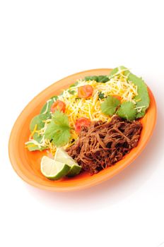 ropa vieja, a Cuban meal, on an orange plate with a healthy salad on a white background