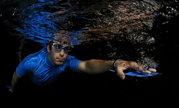 Man swimming underwater in pool with resistance swim paddles for exercise