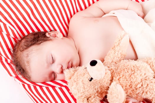 sleeping cute little baby on red and white stripes pillow with teddy bear