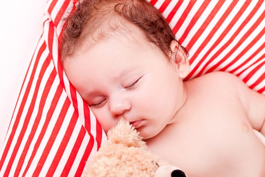 sleeping cute little baby on red and white stripes pillow with teddy bear
