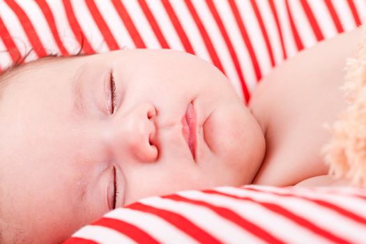 sleeping cute little baby on red and white stripes pillow with teddy bear