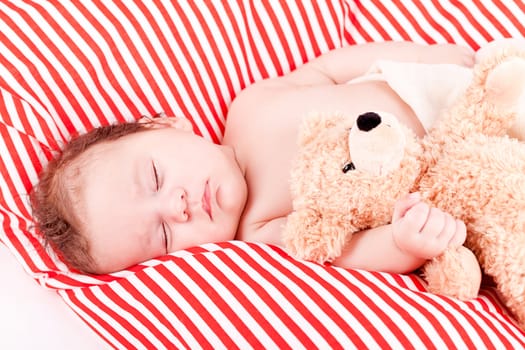 sleeping cute little baby on red and white stripes pillow with teddy bear