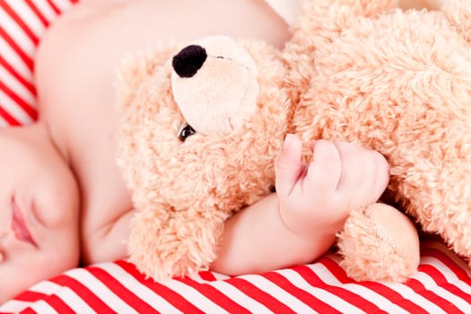 sleeping cute little baby on red and white stripes pillow with teddy bear