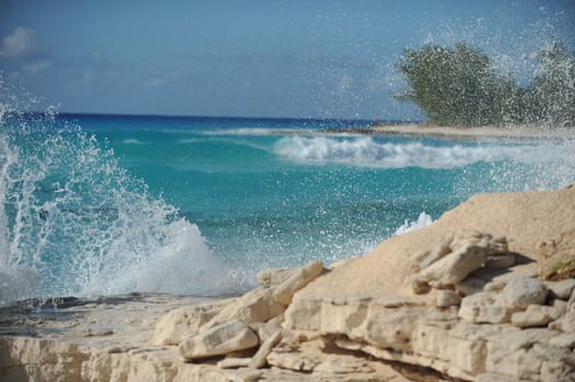 Waves crashing agains rocks in the Bahamas with the beach in the background