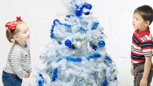 two beautiful happy children playing near christmas tree