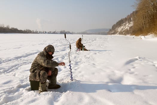 The fisherman on winter fishing in frosty day