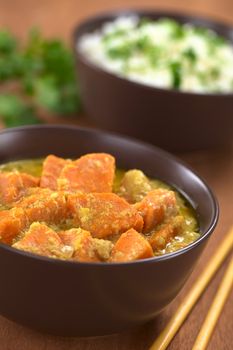 Bowl of vegetarian sweet potato and coconut curry with cooked rice in the back (Selective Focus, Focus one third into the curry)