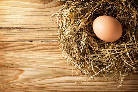 Egg in hay nest on old wooden table background, top view