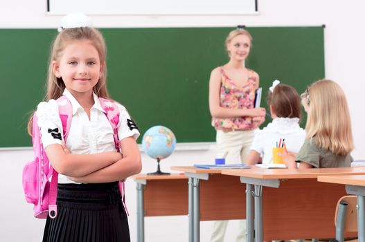 portrait of schoolgirl with a school backpack, in the background a classroom and the teacher tells the class