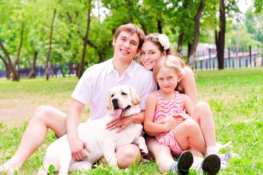 Happy young family with Labrador is resting in the park