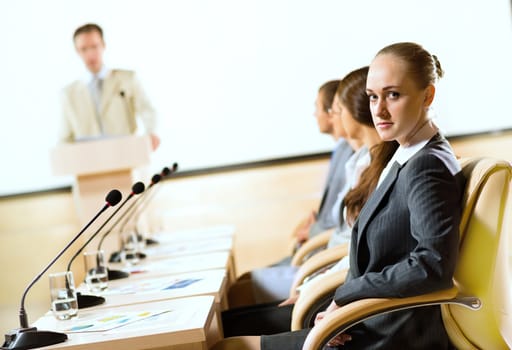 group of business people sitting at the tables at the presentation, woman looking at the camera